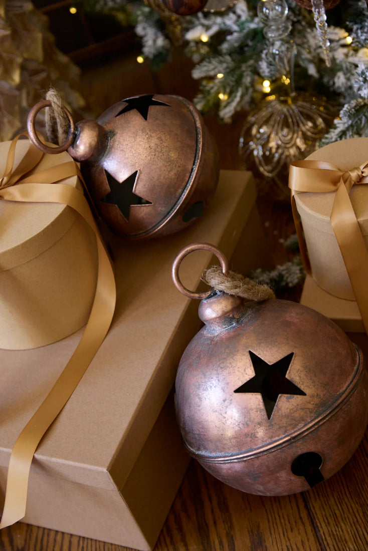 Decorative copper bells with star cutouts on a wooden surface with Christmas decorations.