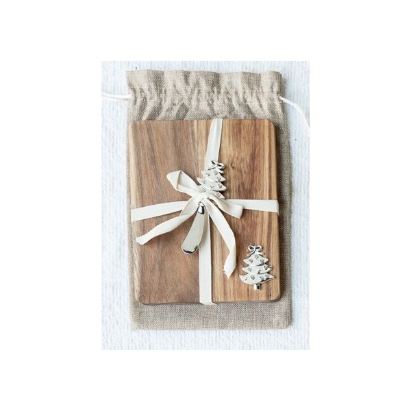 An acacia wood cheeseboard with a white spreader and a decorative Christmas tree-shaped sprinkler on top, tied with a string and presented in a burlap gift bag.